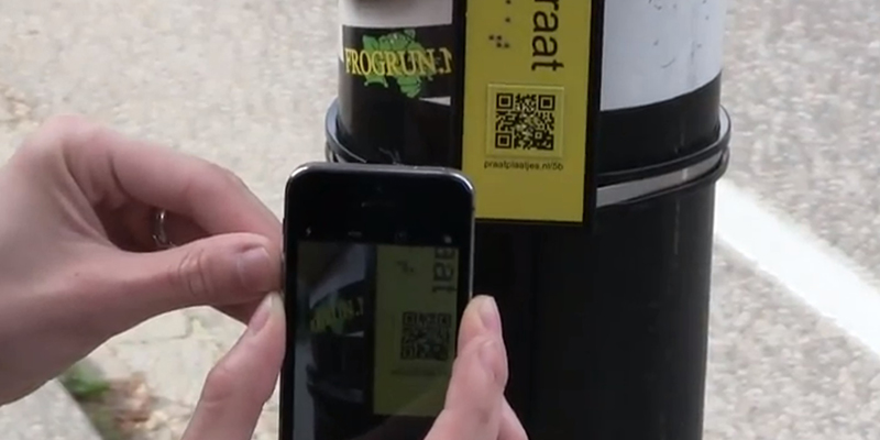 met een smartphone wordt een QR-code gescand op een straatnaambordje waar ook braille op staat