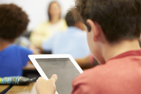 Jongen werkt met tablet terwijl hij in de klas zit.