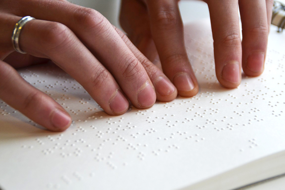 Twee handen voelen een pagina met braille