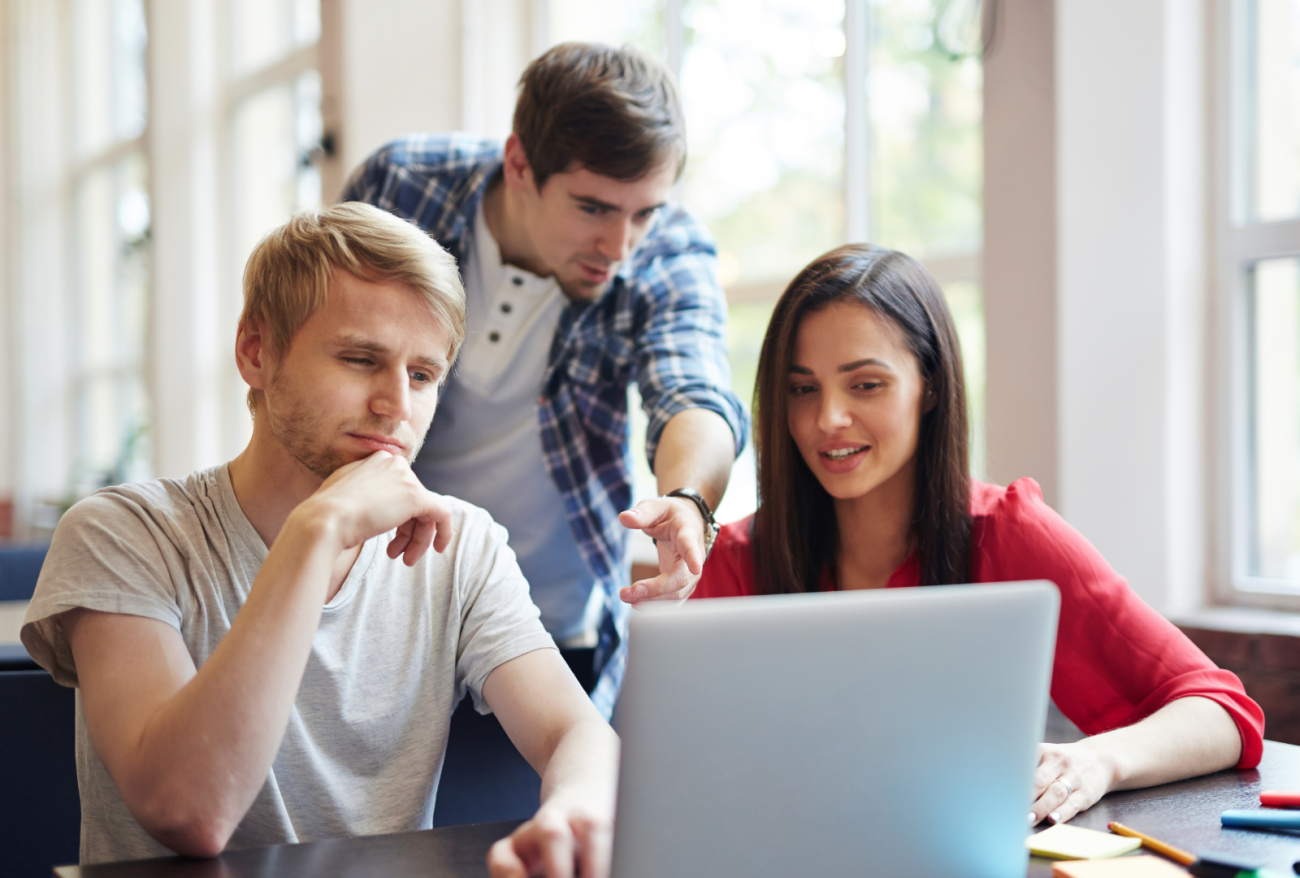 afbeelding van een jongeman die aan twee mensen iets uitlegt, wijzend op een laptop