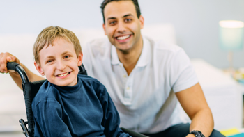 kind in rolstoel met daarachter begeleider