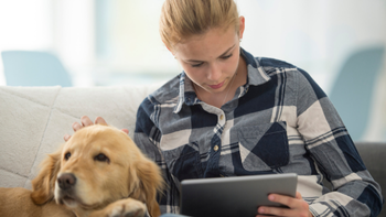 jong persoon leest op ipad met hond naast zich