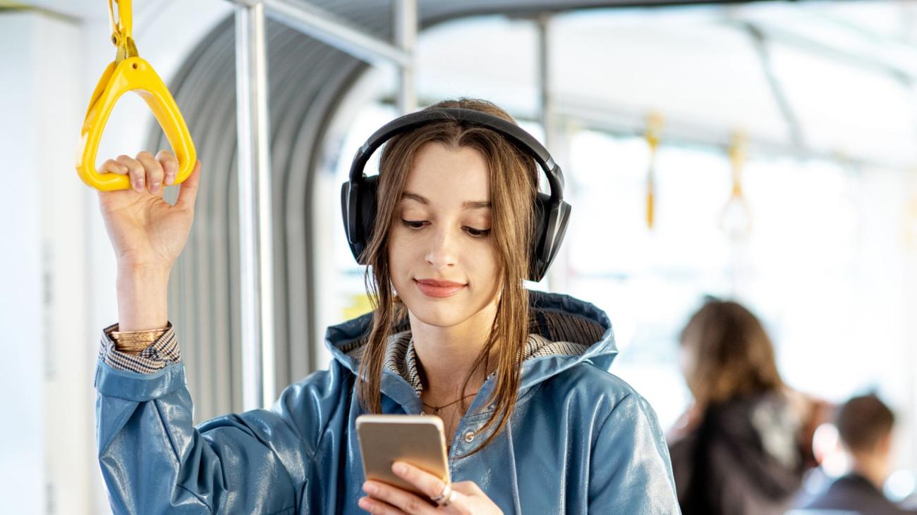 reiziger met koptelefoon en kijkend op mobiele telefoon in de tram