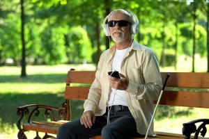 blinde man beluistert zijn smartphone op een bankje in een park